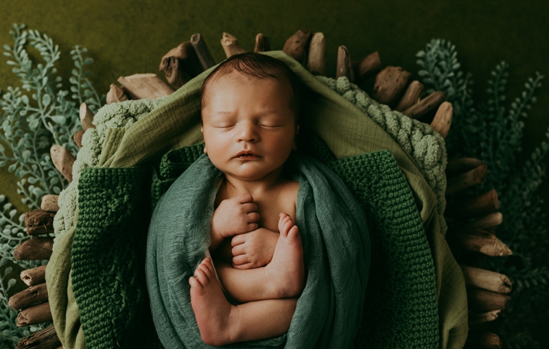 Newborn Photographer, a baby is wrapped in blankets and sleeps in a basket