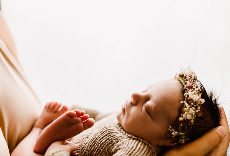 Newborn Photographer, mother holds new daughter in arms, baby wears a floral crown