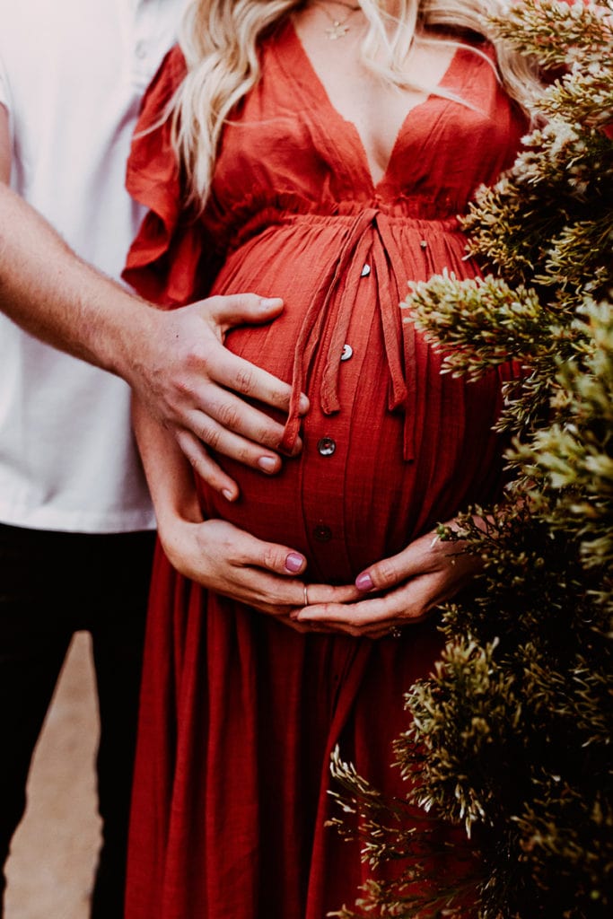 Maternity Photographer, an expecting mother stands with her partner, all hands on her belly