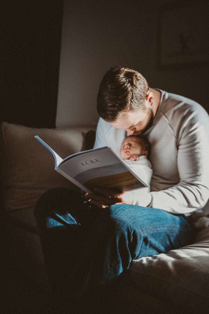 Newborn Photographer, A father reads to his baby on the couch